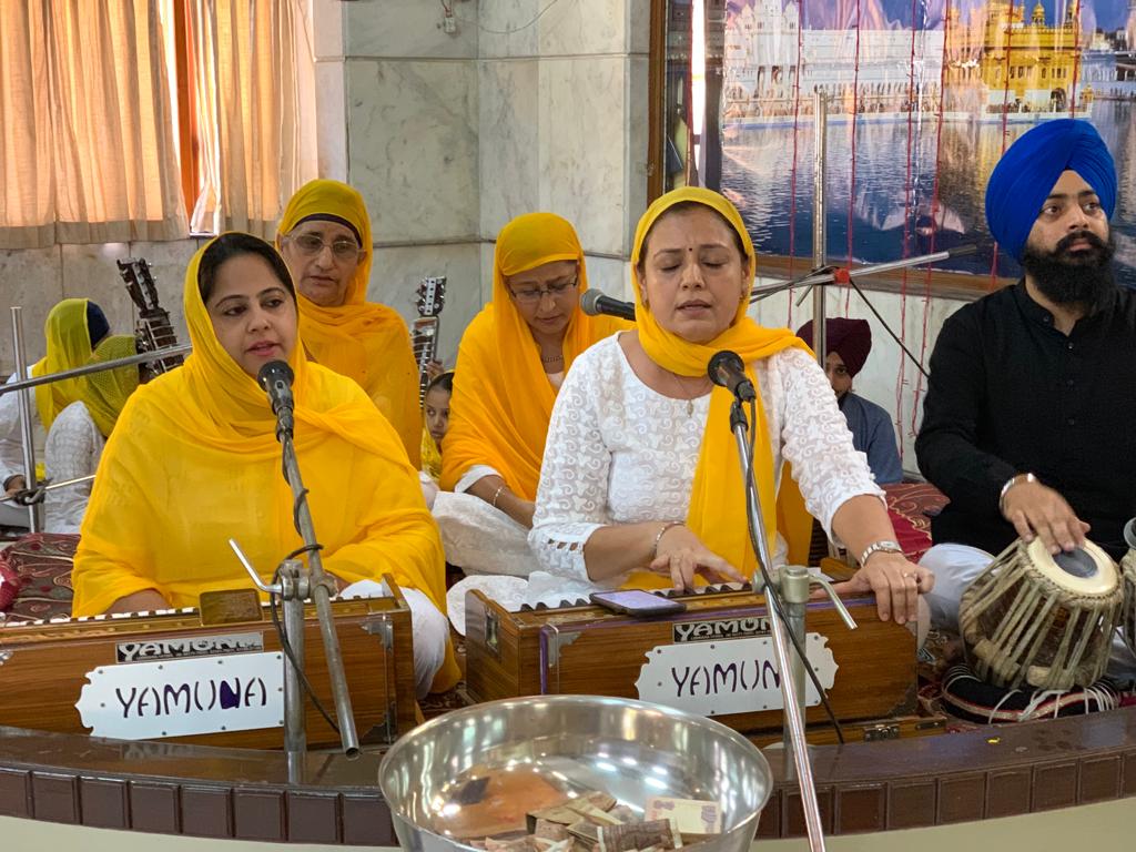Women and men singing kirtan with harmoniums and a tabla