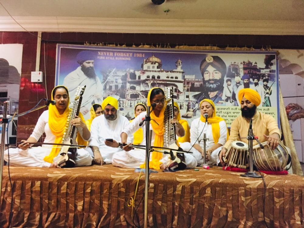 Group of musicians seated on a stage performing kirtan