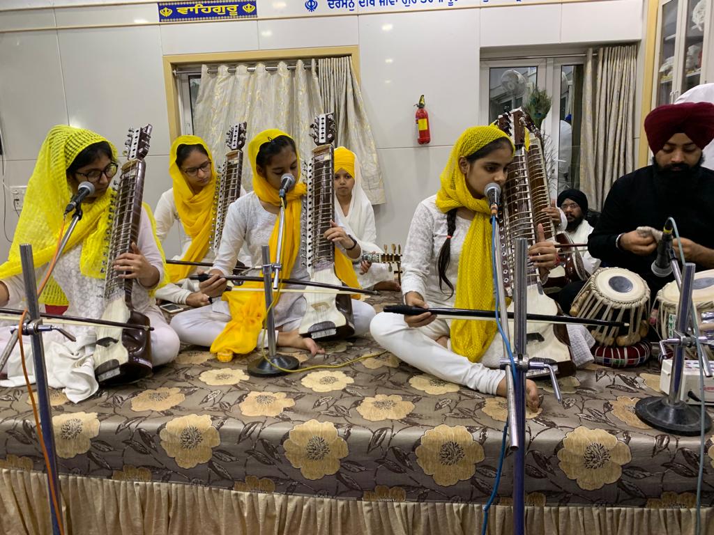 Girls with stringed instruments and a tabla player performing on stage